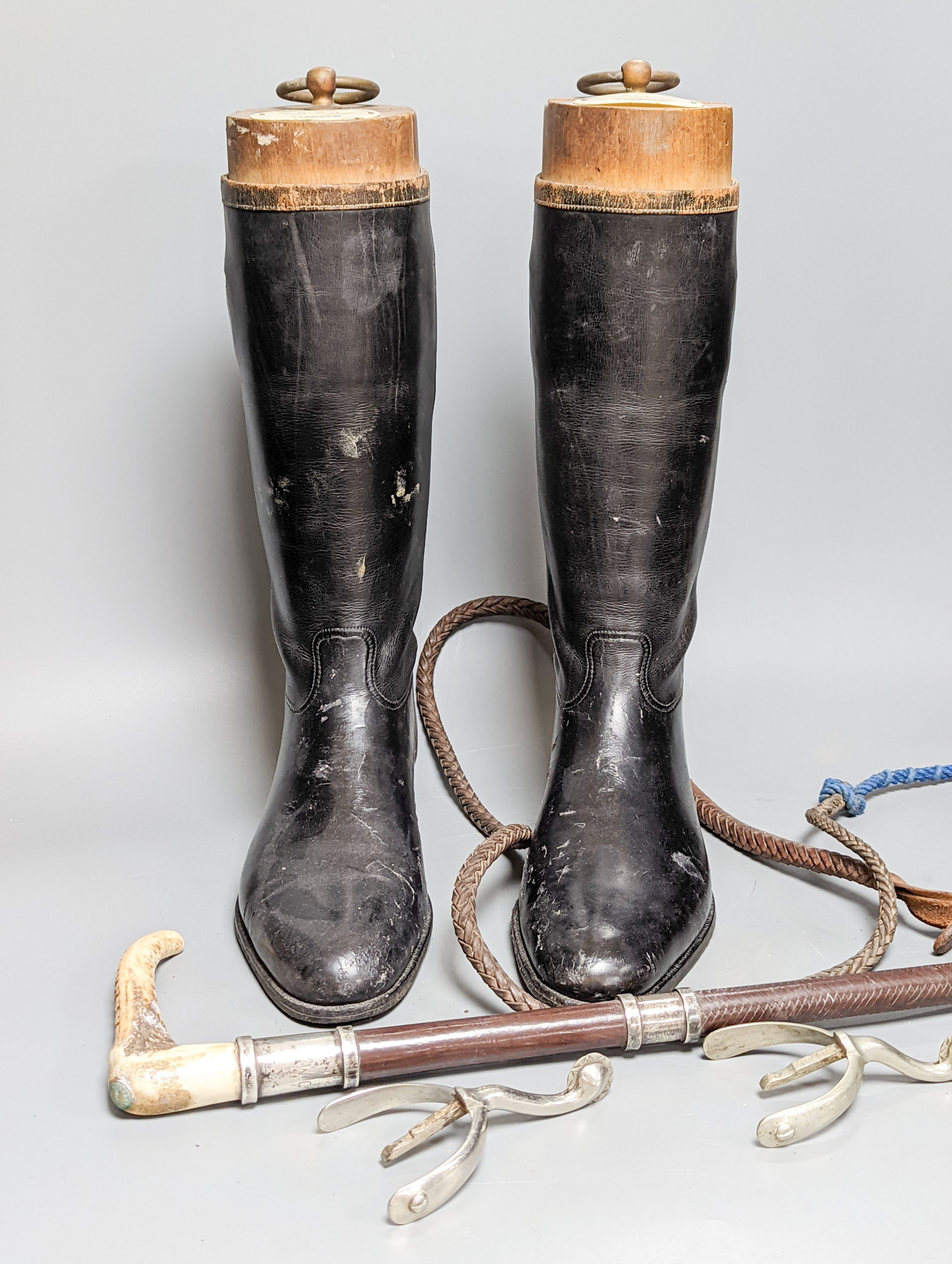 A pair of black leather riding boots with trees, a silver mounted whip and spurs